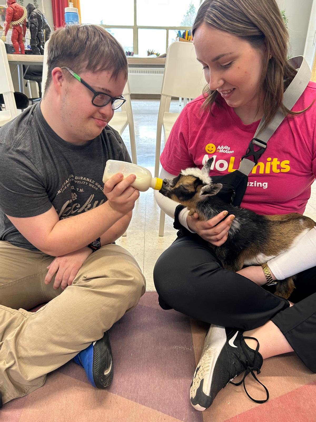 A member and a staff member bottle-feed a baby goat at the Kitchener–Waterloo day program.